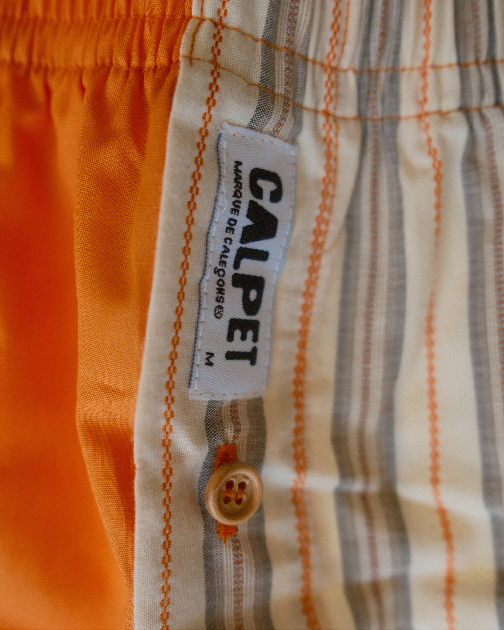 gros plan sur la braguette rayee, le bouton en bois et l'étiquette CALPET du caleçon parachute orange